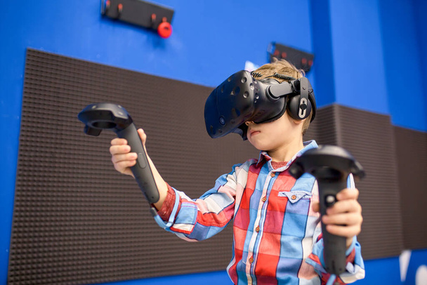 tecnología moderna, juegos y concepto de personas - niño en auriculares de realidad virtual o gafas 3D jugando videojuegos en el centro del juego
 - Foto, Imagen
