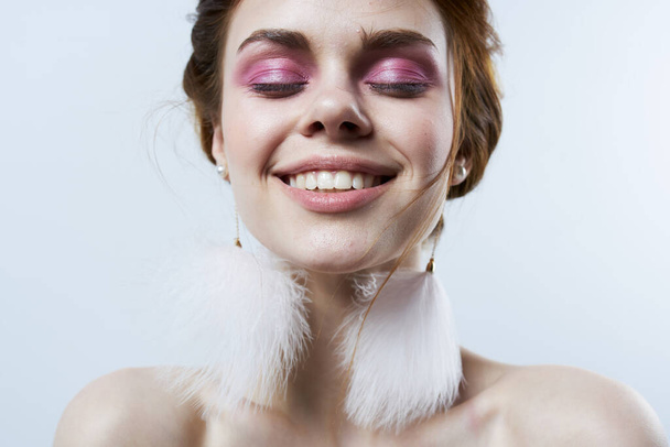 vrouw met heldere make-up pluizig oorbellen kale schouders close-up - Foto, afbeelding