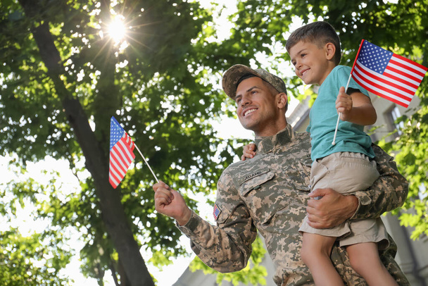 Soldier and his little son with American flags outdoors, low angle view. Veterans Day in USA - Фото, зображення