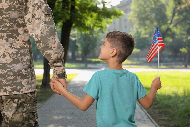 Soldier and his little son with American flag outdoors, back view. Veterans Day in USA - Фото, изображение