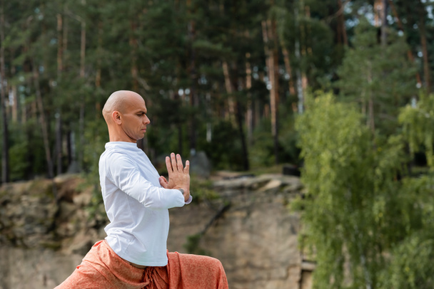 πλαϊνή άποψη του βουδιστής σε λευκό φούτερ διαλογισμό με προσεύχεται τα χέρια στο δάσος - Φωτογραφία, εικόνα