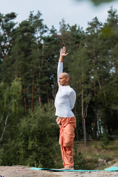 buddhist in harem pants and sweatshirt practicing yoga with raised hand outdoors - Fotó, kép