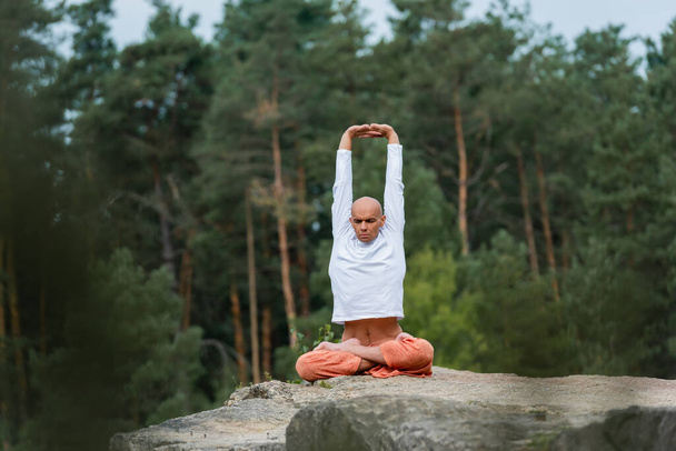buddhist meditating in yoga pose with raised hands outdoors on blurred foreground - Photo, Image