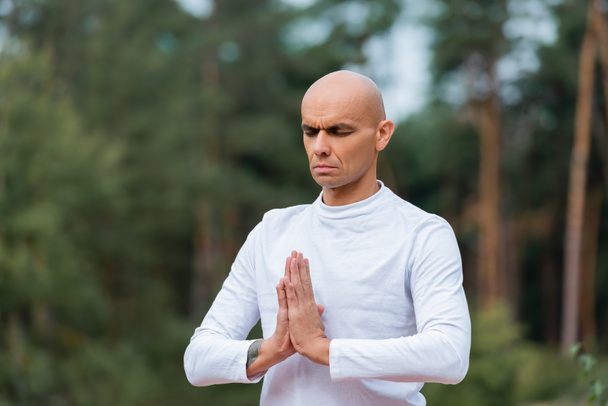 buddhist in sweatshirt praying with closed eyes outdoors - Photo, Image