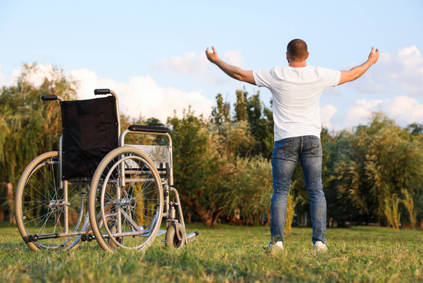 Man standing near wheelchair on sunny day, back view. Healing miracle - Foto, Imagem