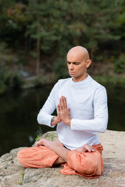 buddhist with closed eyes and praying hands meditating in lotus pose outdoors - Fotó, kép