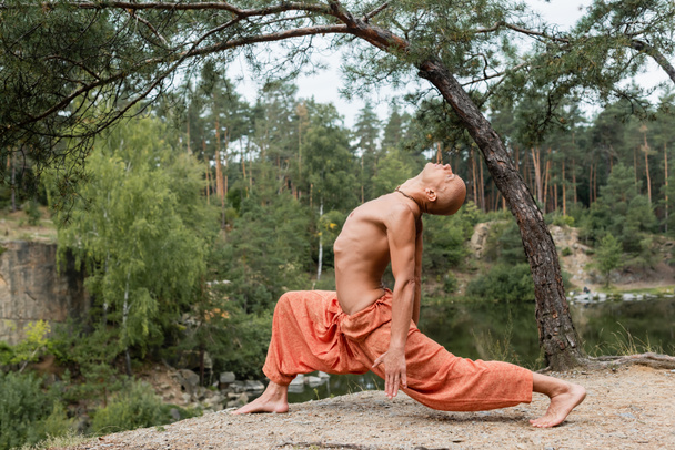 Seitenansicht des hemdslosen buddhistischen Meditierenden in Ausfallpose im Freien - Foto, Bild