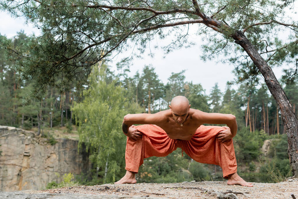 shirtloze boeddhist in harem broek praktiserend godin pose in bos - Foto, afbeelding