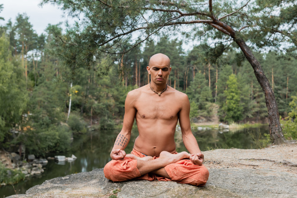 tatuado, sem camisa budista meditando em pose de lótus com os olhos fechados ao ar livre - Foto, Imagem