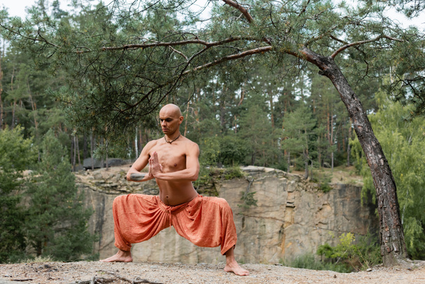 buddista senza maglietta in pantaloni harem meditando in posa dea con le mani in preghiera nella foresta - Foto, immagini