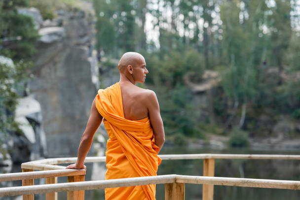 back view of buddhist standing near wooden fence in forest and looking away - Photo, Image
