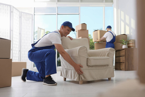 Moving service employees with armchair and cardboard boxes in room - Фото, зображення