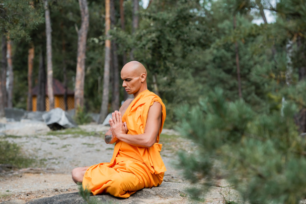 moine bouddhiste en robe orange méditant les yeux fermés en pose de lotus - Photo, image