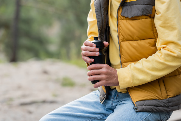 cropped view of tourist in warm vest opening thermo bottle outdoors - Foto, Imagem