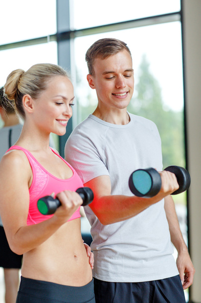 smiling young woman with personal trainer in gym - Photo, Image