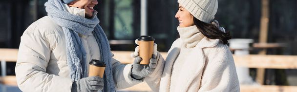 happy young man giving paper cup to cheerful girlfriend in winter hat, banner - Photo, Image