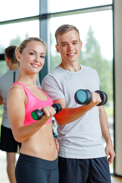 Lächelnde junge Frau mit Personal Trainer im Fitnessstudio - Foto, Bild
