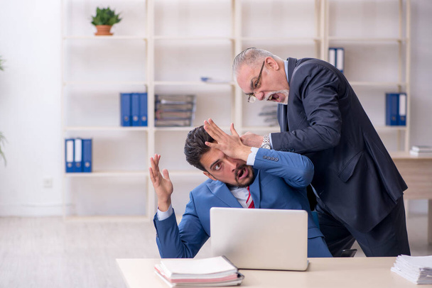 Old boss and young male employee in bullying concept - Foto, afbeelding