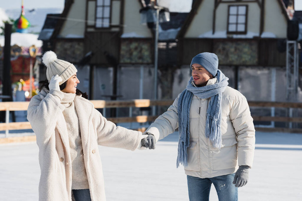 アイスリンクでスケートをしながら手を取り合う若い陽気なカップル  - 写真・画像