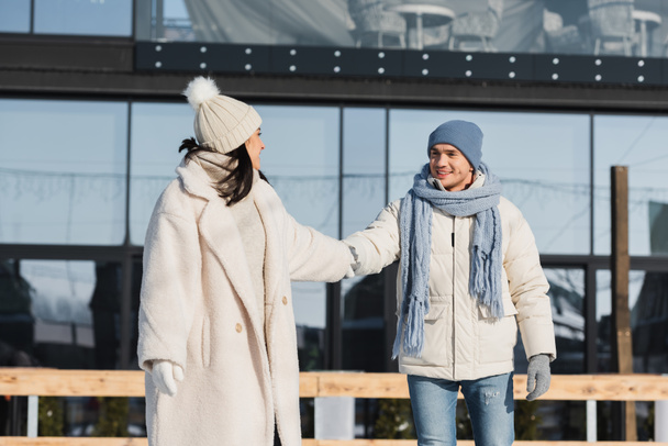 young and positive couple holding hands while skating on ice rink  - Photo, Image