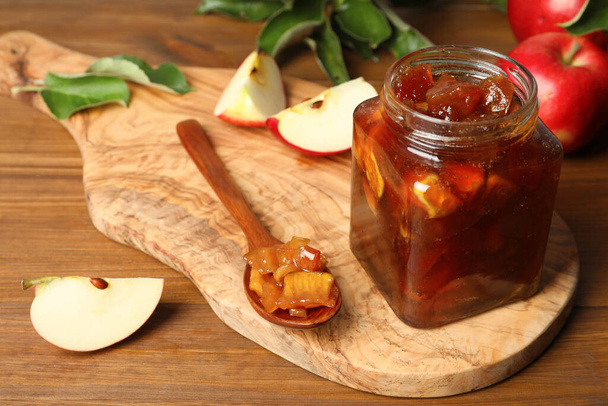Tasty apple jam in glass jar and fresh fruits on wooden table, space for text - Photo, image