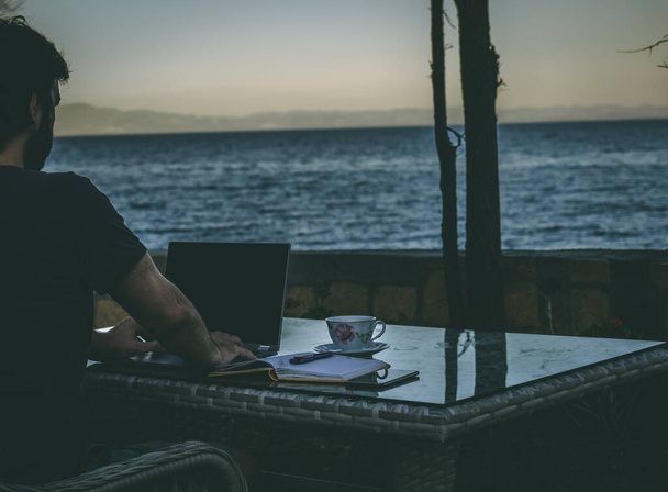 Concept d'un homme d'affaires indépendant professionnel travaillant à partir d'un ordinateur portable depuis une maison d'été en vacances, travaillant à distance en vacances, mobilité avec la technologie - Photo, image