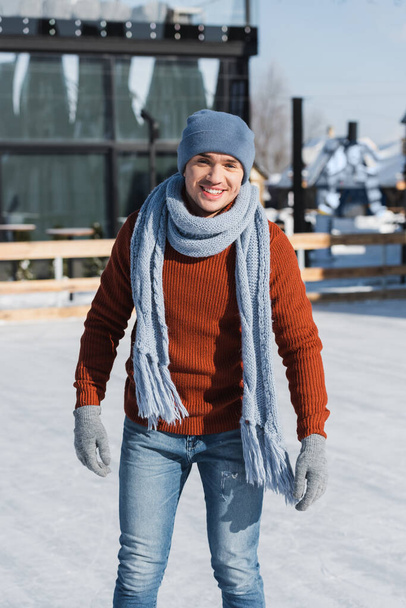 happy young man in sweater, scarf and winter hat skating on ice rink - Photo, Image