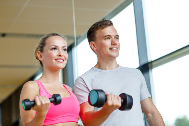 smiling young woman with personal trainer in gym - Фото, зображення