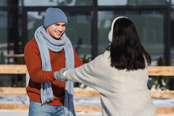 boldog férfi kalapban nézi elmosódott barátnő miközben fogja a kezét a jégpályán  - Fotó, kép