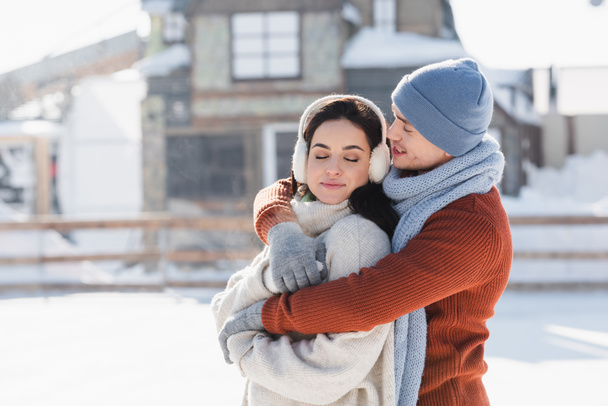 happy man hugging young woman in ear muffs on ice rink  - Fotografie, Obrázek