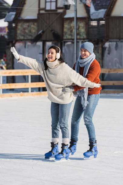 full length of happy man supporting excited woman skating on ice rink  - Foto, imagen