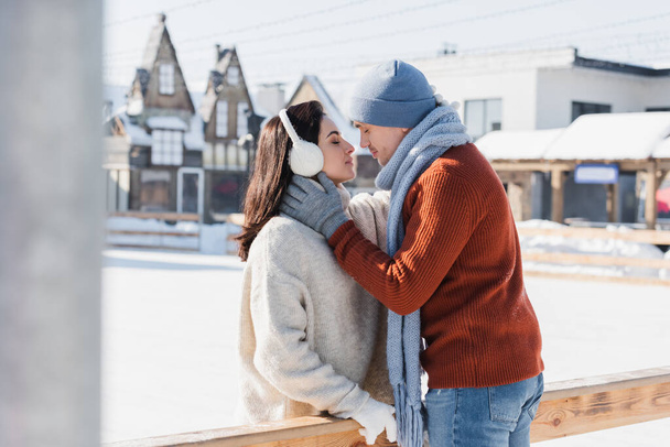 side view of couple kissing near wooden border on ice rink  - 写真・画像