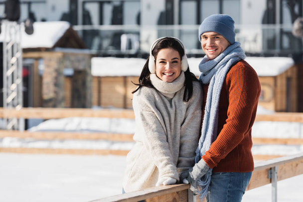 happy man and woman standing near wooden border on skating rink - Φωτογραφία, εικόνα