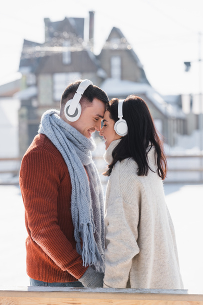 Seitenansicht eines lächelnden Paares, das sich umarmt, während es draußen über Kopfhörer Musik hört  - Foto, Bild