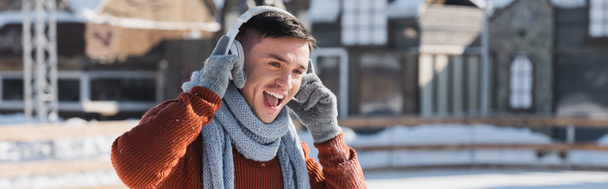 pozitív fiatal férfi pulóverben és sálban zenét hallgat, miközben kint énekel, banner - Fotó, kép