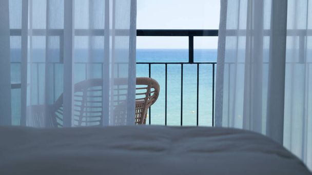 Chambre d'hôtel avec sa propre terrasse et vue sur la mer. Vue sur la mer depuis un lit de chambre à travers des rideaux blancs. Terrasse donnant sur la mer par une journée ensoleillée.  - Photo, image