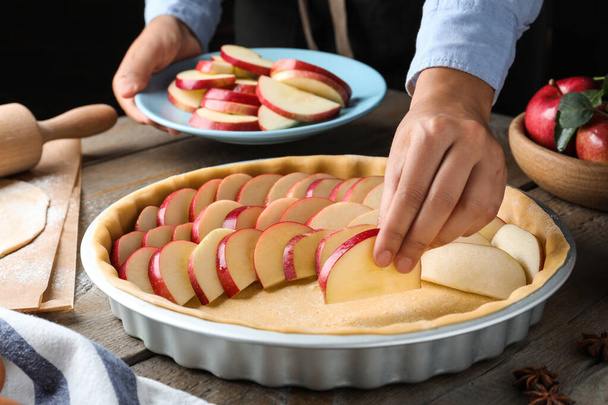 Woman putting apple slices into dish with raw dough at wooden table, closeup. Baking pie - Фото, зображення