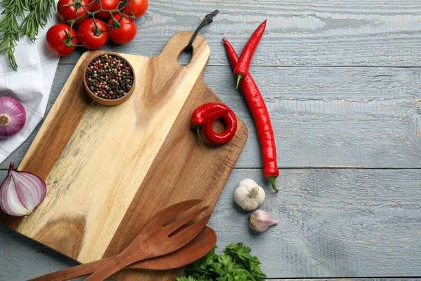 Cutting board and vegetables on grey wooden table, flat lay with space for text. Cooking utensils - Fotoğraf, Görsel