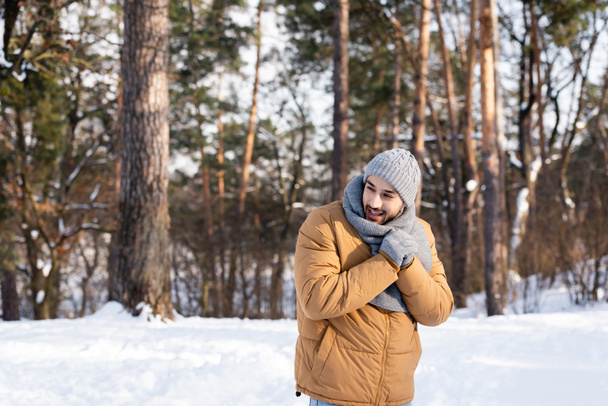 Lächelnder Mann in warmer Kleidung steht im Winterpark  - Foto, Bild