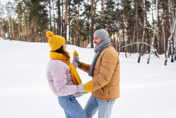 Zijaanzicht van vrolijke coupe in winteroutfit dansen in snowy park  - Foto, afbeelding