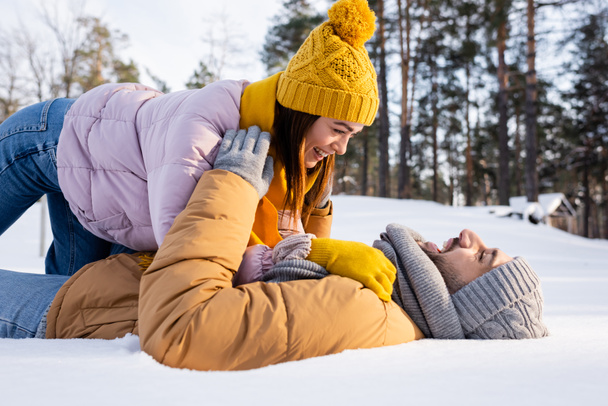 Oldalnézet vidám férfi feküdt a hó közelében barátnője téli ruhában  - Fotó, kép
