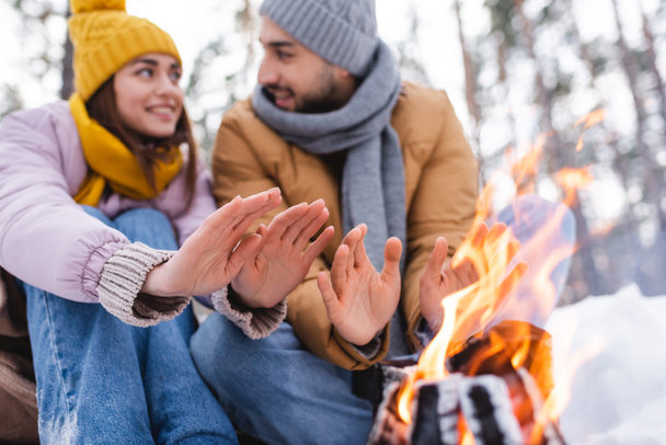 Bonfire near blurred couple warming hands in winter park  - Photo, Image