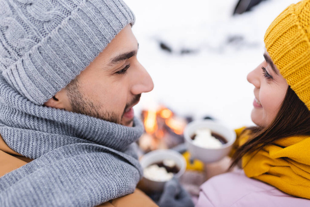 Smiling couple in knitted hats looking at each other in winter park  - Foto, Imagen
