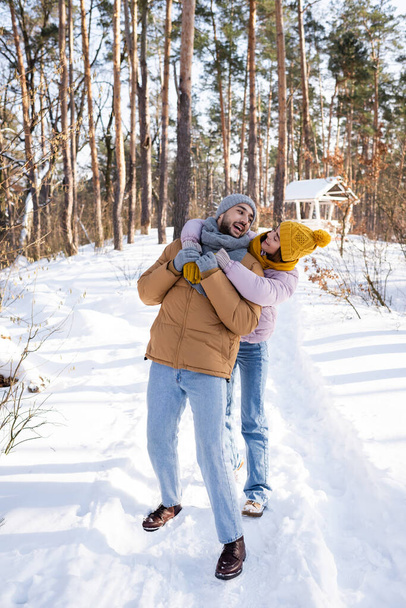 Улыбающаяся женщина обнимает парня в шарфе и шляпе в снежном парке  - Фото, изображение