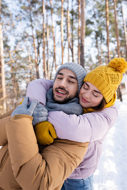 Young woman hugging boyfriend with closed eyes in winter park  - Foto, Imagen