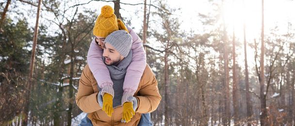 Cheerful woman piggybacking on boyfriend in winter park, banner  - Fotó, kép