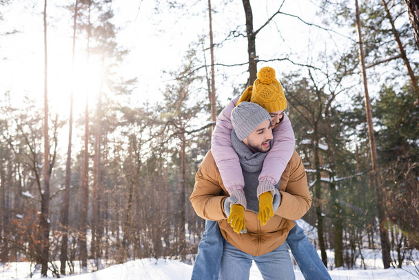Ευτυχισμένος γυναίκα pigggybacking για φίλο στο χειμώνα στολή στο πάρκο  - Φωτογραφία, εικόνα