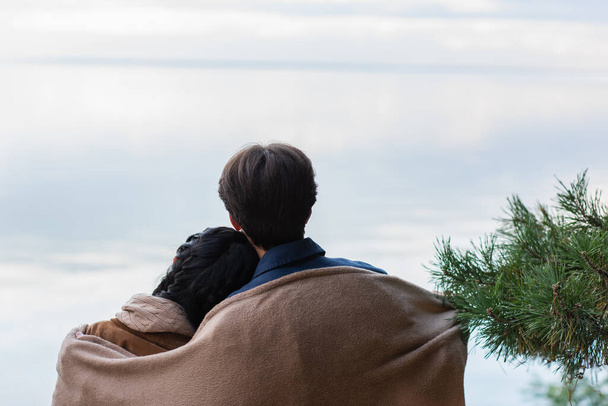 Задний вид на пару в одеяле, стоящую у озера осенью  - Фото, изображение