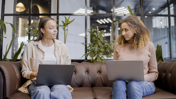 Two women talking, typing on laptops in office, female IT specialists at work - Фото, зображення