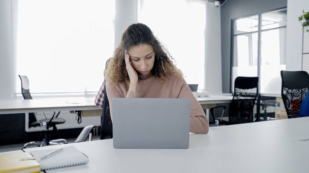 Молода жінка, яка має головний біль на робочому місці, працює на ноутбуці в офісі, погано себе почуває
 - Фото, зображення
